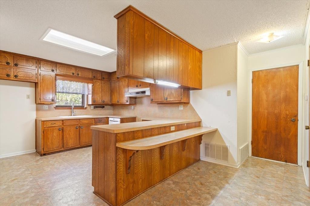 208 South Hedwig Street Riesel, TX 76682 - Photo 13 of 31 Kitchen featuring brown cabinetry, light countertops, a breakfast bar, a peninsula, and ornamental molding