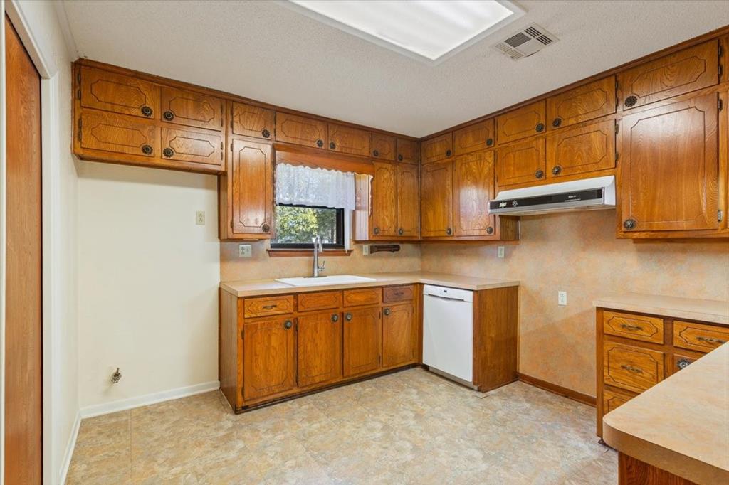 208 South Hedwig Street Riesel, TX 76682 - Photo 14 of 31 Kitchen with brown cabinetry, light countertops, dishwasher, and under cabinet range hood