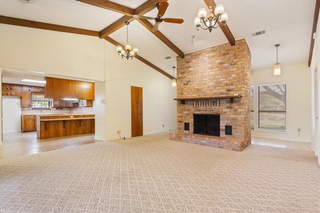 208 South Hedwig Street Riesel, TX 76682 - Photo 9 of 31 Unfurnished living room with high vaulted ceiling, beamed ceiling, a chandelier, a brick fireplace, and light carpet