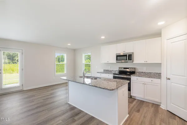 a kitchen with stainless steel appliances granite countertop a stove a sink a refrigerator white cabinets and wooden floor