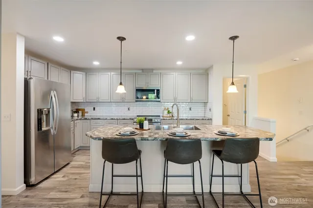 a kitchen with stainless steel appliances kitchen island granite countertop a dining table chairs and white cabinets