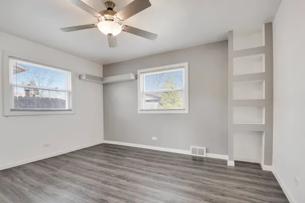 a view of an empty room with wooden floor and a ceiling fan