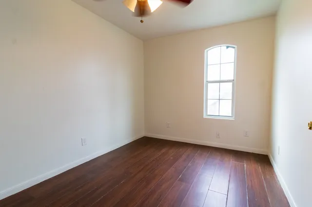 an empty room with wooden floor chandelier fan and windows