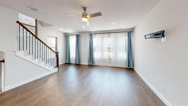 an empty room with wooden floor fan and windows