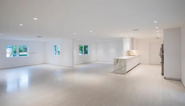 a view of an empty room with kitchen and window