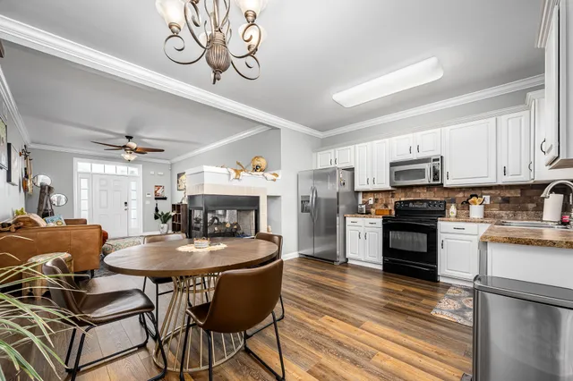 a kitchen with stainless steel appliances granite countertop a stove a refrigerator a kitchen island a dining table and chairs with wooden floor