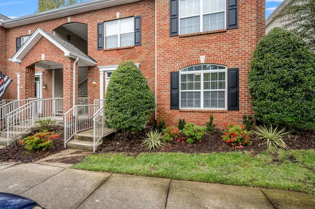 a view of a brick house with plants and large tree