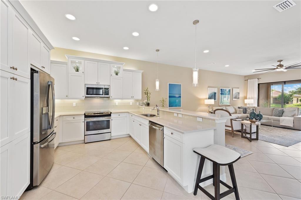 13338 Coronado Drive Naples, FL 34109 - Photo 4 of 22 a kitchen with stainless steel appliances kitchen island granite countertop a refrigerator a stove a sink a dining table and chairs with wooden floor