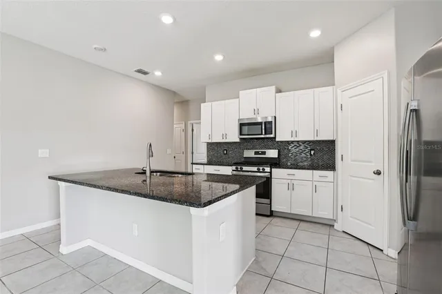 a kitchen with stainless steel appliances granite countertop a sink a stove a refrigerator and white cabinets