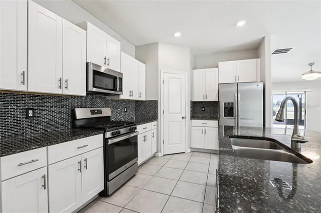 a kitchen with stainless steel appliances granite countertop a refrigerator a stove a sink and white cabinets