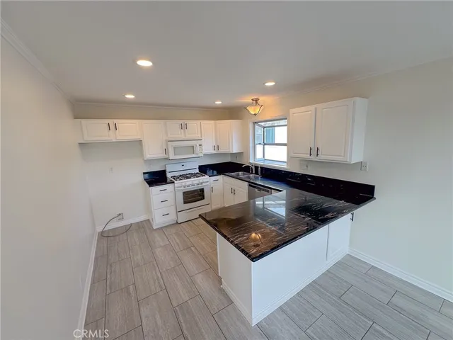 a kitchen with stainless steel appliances granite countertop a sink a stove a refrigerator and white cabinets