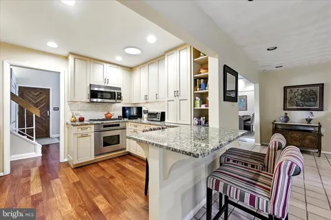 a kitchen with stainless steel appliances granite countertop a stove top oven a sink a refrigerator white cabinets and wooden floor