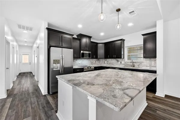 a large kitchen with stainless steel appliances kitchen island a large counter top and wooden floor