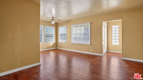 an empty room with wooden floor windows and chandelier fan