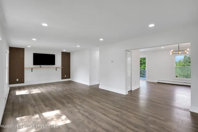 a view of an empty room with wooden floor and a kitchen
