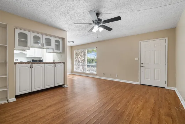 an empty room with wooden floor chandelier fan and windows