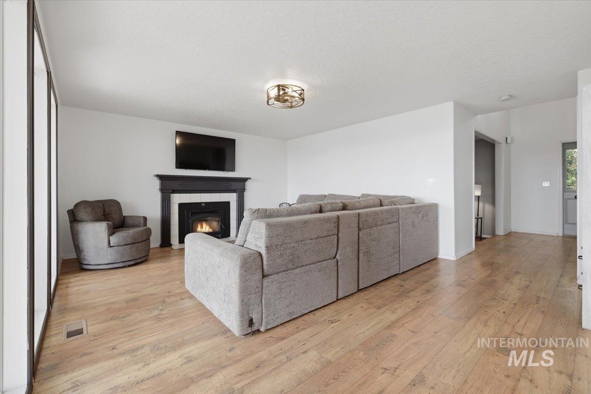 24440 Kenridge Road Caldwell, ID 83607 - Photo 21 of 48 Living space featuring a fireplace with a dark wood mantel and white surround, wood-finish flooring, white walls, and a contemporary ceiling light fixture