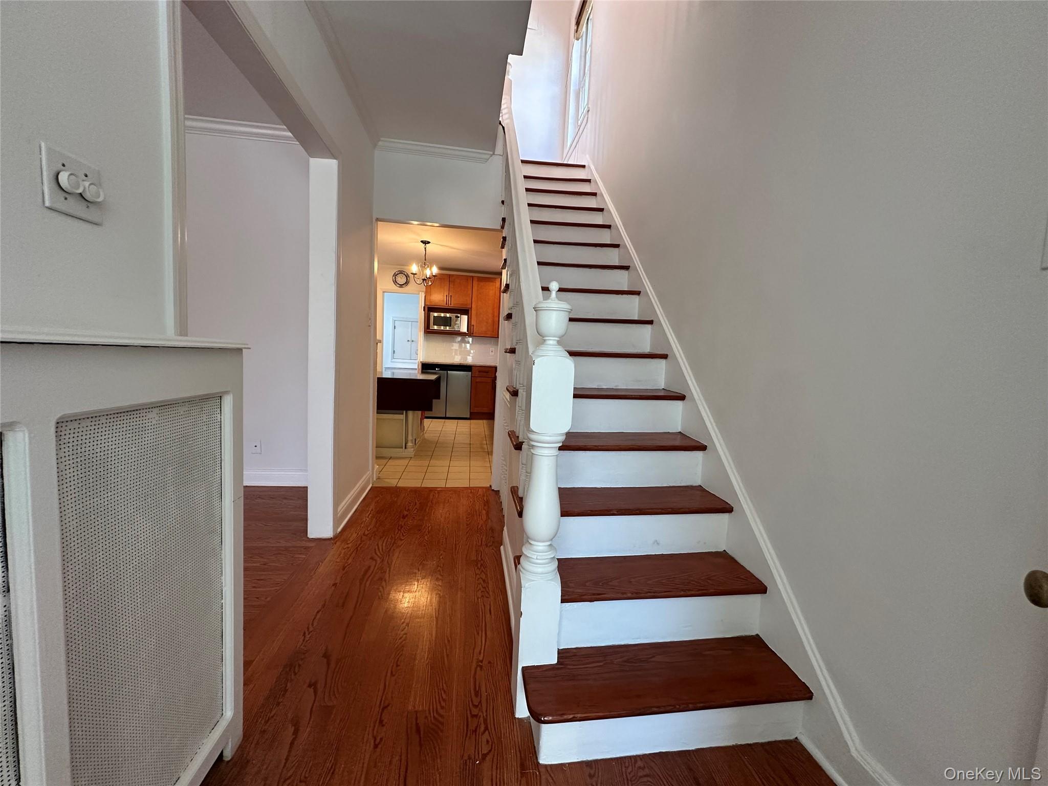 197 Johnson Road Scarsdale, NY 10583 - Photo 21 of 36 Stairway featuring crown molding, wood-type flooring, and a notable chandelier