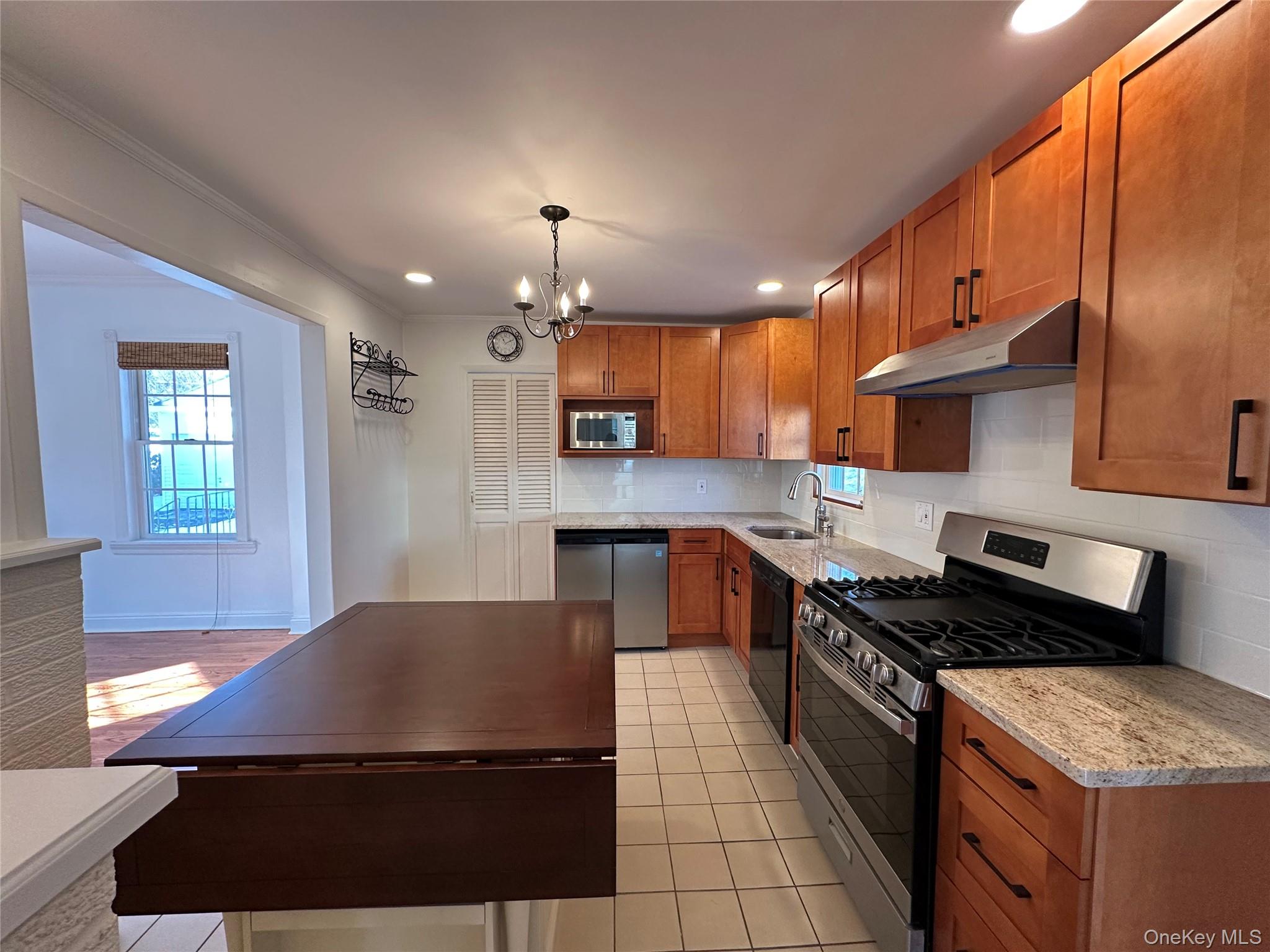 197 Johnson Road Scarsdale, NY 10583 - Photo 22 of 36 Eat-In Kitchen with Island featuring sink, light tile patterned floors, appliances with stainless steel finishes, hanging light fixtures, and backsplash