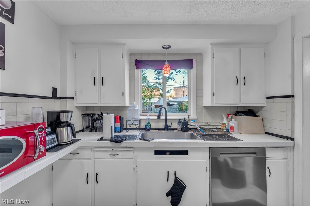 3962 Grosvenor Road South Euclid, OH 44118 - Photo 11 of 27 Kitchen space featuring white cabinetry with black hardware, a stainless steel sink with a matte black faucet, and a built-in stainless steel dishwasher