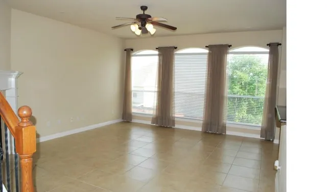 an empty room with a chandelier fan and windows