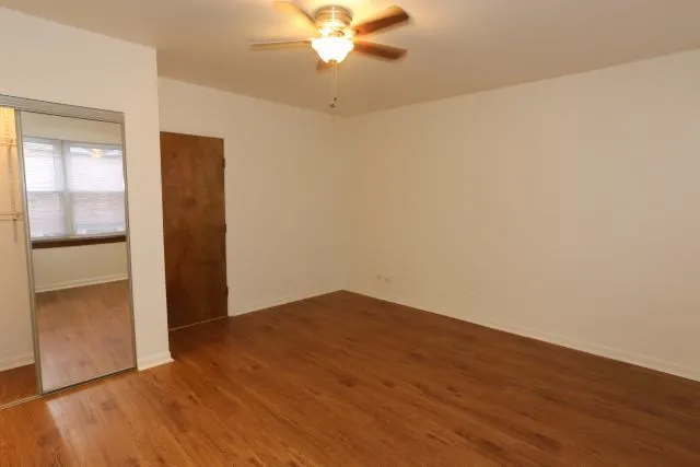 an empty room with wooden floor fan and windows