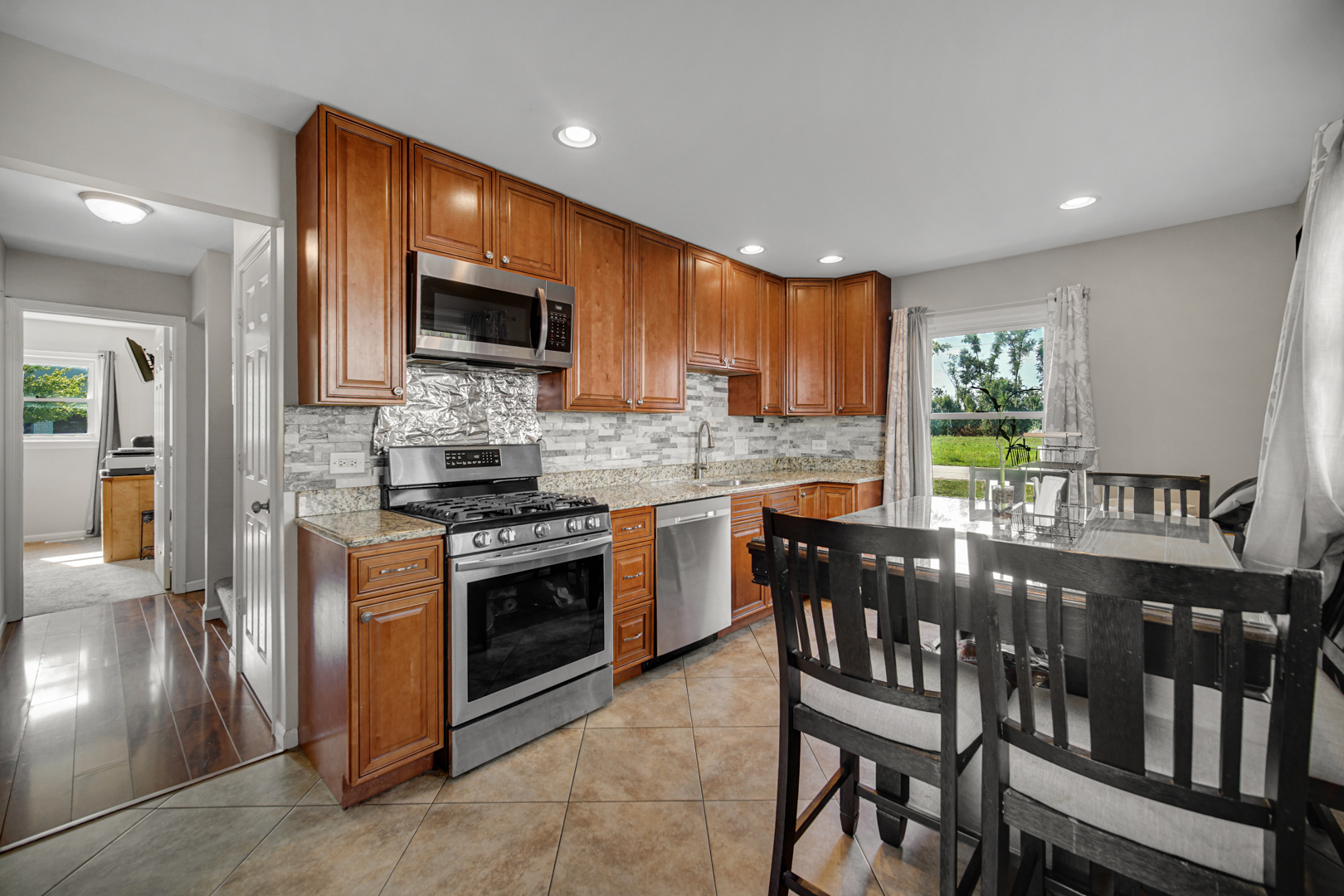 25W277 Doris Avenue Carol Stream, IL 60188 - Photo 7 of 27 a kitchen with stainless steel appliances granite countertop wooden floor a stove a sink dishwasher a dining table and chairs