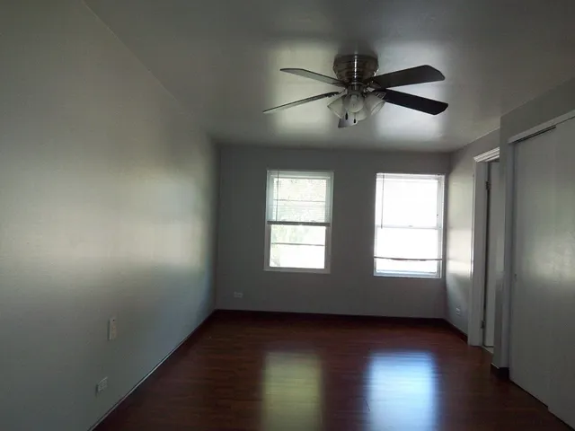 an empty room with wooden floor fan and windows
