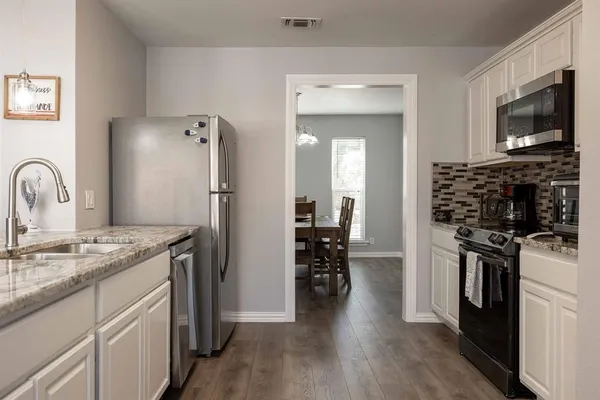 a kitchen with stainless steel appliances granite countertop a refrigerator a sink dishwasher a dining table and chairs with wooden floor