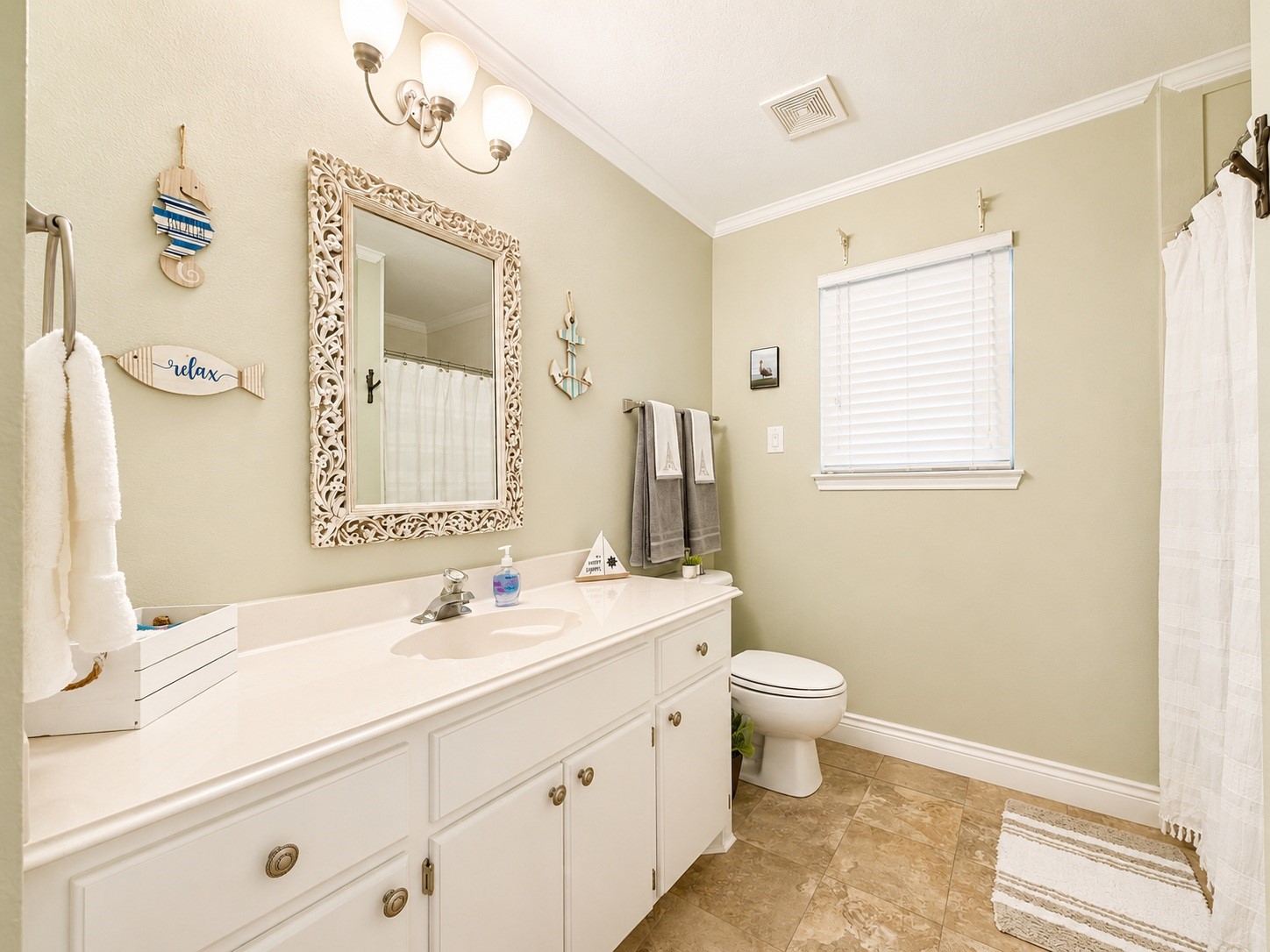 135 Sand Shoals Road Freeport, TX 77541 - Photo 16 of 20 This bathroom features a classic design with a neutral color palette, a large vanity with ample storage, decorative wall accents, and a combination of tile flooring and a window for natural light.
