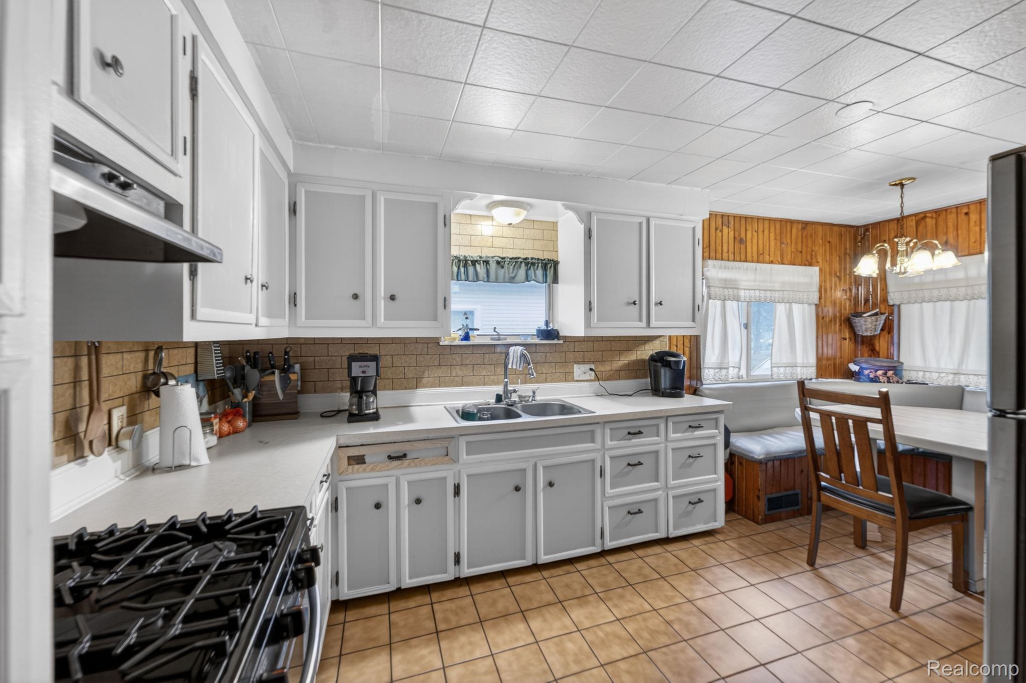 304 West Ridge Street Owosso, MI 48867 - Photo 18 of 45 Kitchen featuring light countertops, black gas range, a chandelier, white cabinetry, and extractor fan