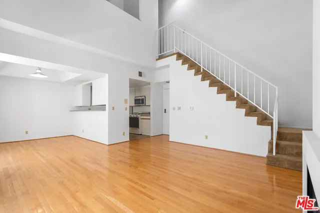 a view of empty room with wooden floor and kitchen