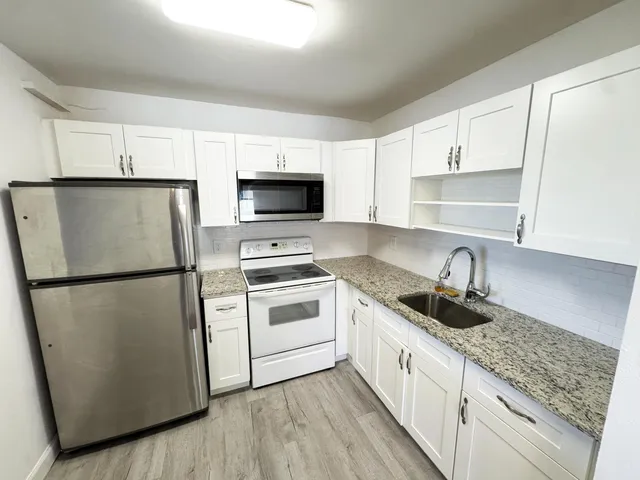 a kitchen with a refrigerator a stove a sink and white cabinets