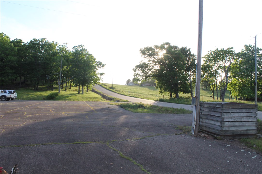 Paved parking area with visible lines, bordered by mature trees and a sloped grassy terrain