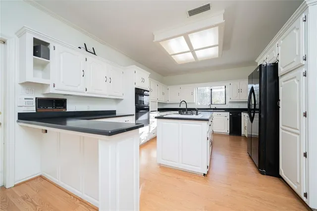 a kitchen with stainless steel appliances kitchen island granite countertop a refrigerator a stove a sink and white cabinets with wooden floor