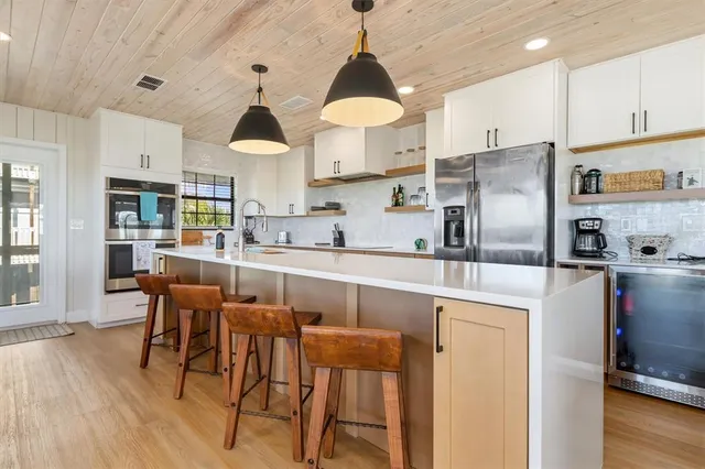 a view of a kitchen with stainless steel appliances granite countertop a refrigerator a oven a sink and a dining table with wooden floor