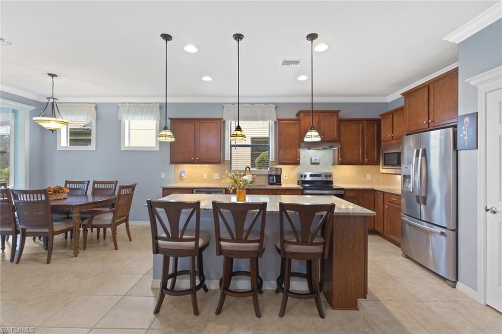 6085 Triumph Lane Ave Maria, FL 34142 - Photo 6 of 42 a kitchen with stainless steel appliances granite countertop a dining table chairs and a refrigerator