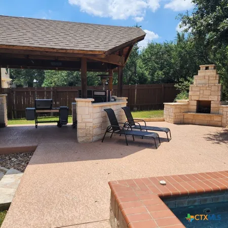 a view of a patio with a table and chairs under an umbrella with a barbeque