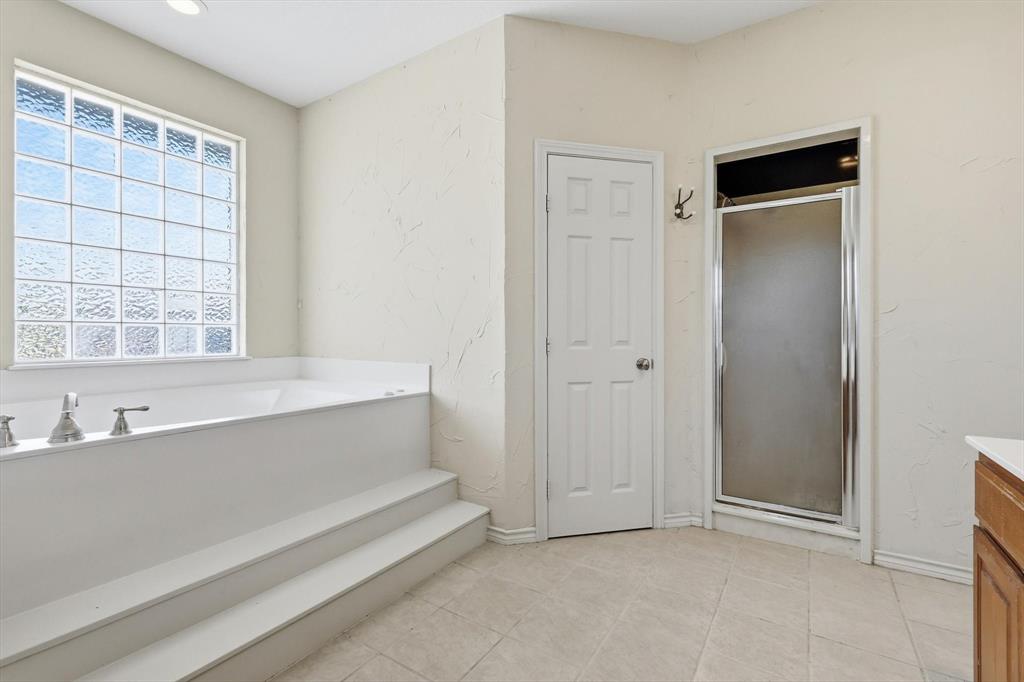 12190 Bell Road Pilot Point, TX 76258 - Photo 25 of 39 Spacious bathroom featuring a built-in soaking tub with steps, a glass block window, chrome fixtures, a separate shower enclosure, and neutral tile flooring