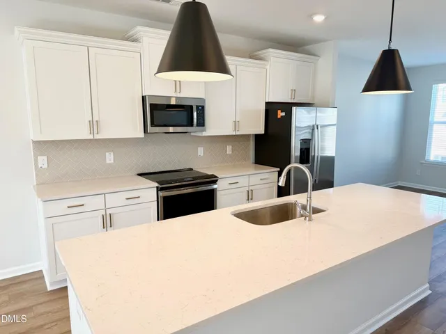 a kitchen with stainless steel appliances a sink a stove a microwave a refrigerator a stove and white cabinets