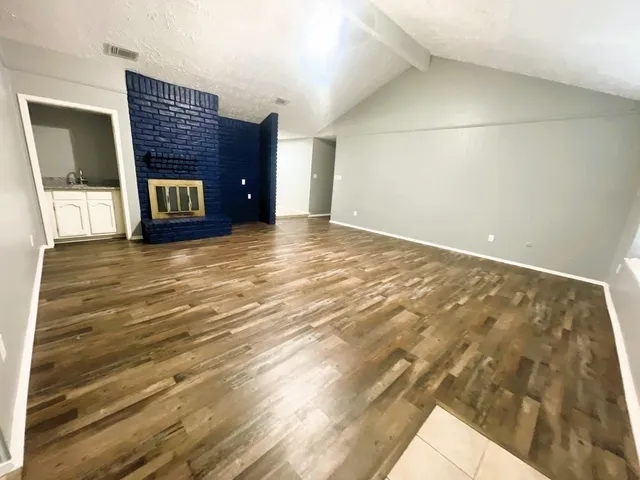 a view of an empty room with wooden floor and a fireplace