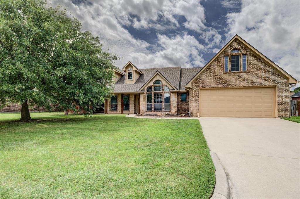 Brick facade home featuring a prominent arched window, a two-car garage, and a large mature tree