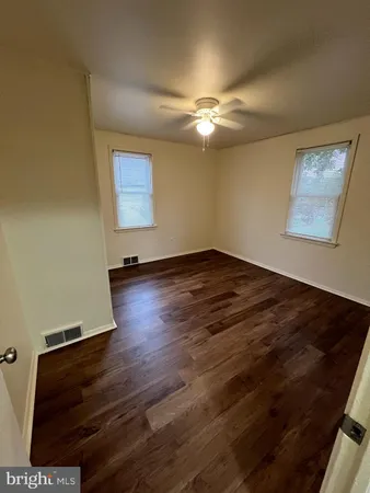a view of an empty room with wooden floor and a ceiling fan