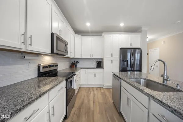 a kitchen with stainless steel appliances granite countertop a refrigerator a sink a stove a microwave a center island and chairs with wooden floor