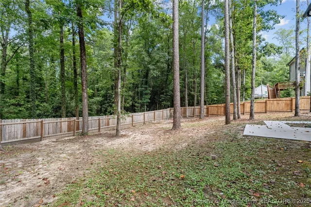 a view of a backyard with large trees and wooden fence