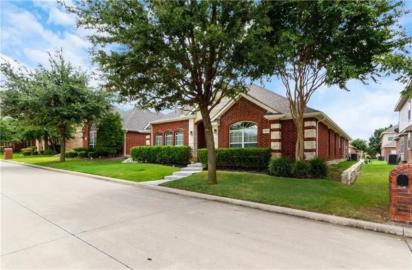 a view of a brick house next to a yard with big trees