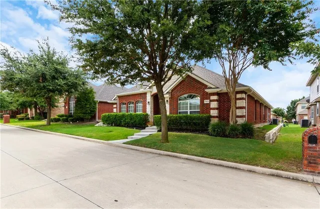 a view of a brick house next to a yard with big trees