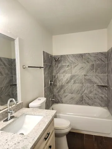 a bathroom with a granite countertop bathtub sink vanity mirror and toilet