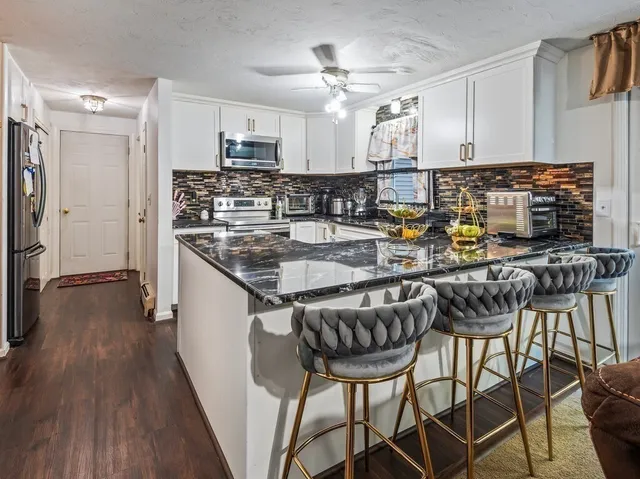 a kitchen with stainless steel appliances granite countertop a stove top oven a refrigerator a sink and chairs