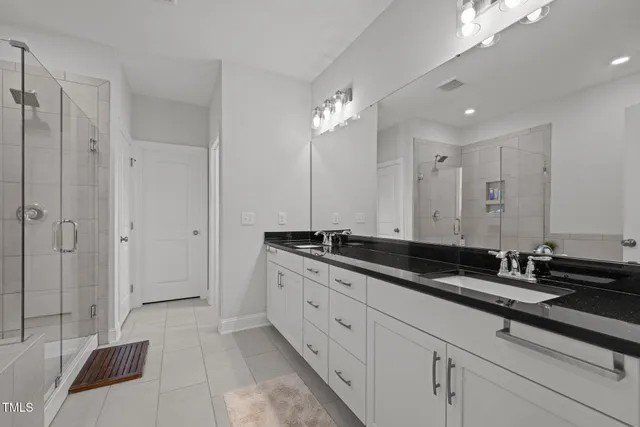 a spacious bathroom with a double vanity sink a large mirror and a shower